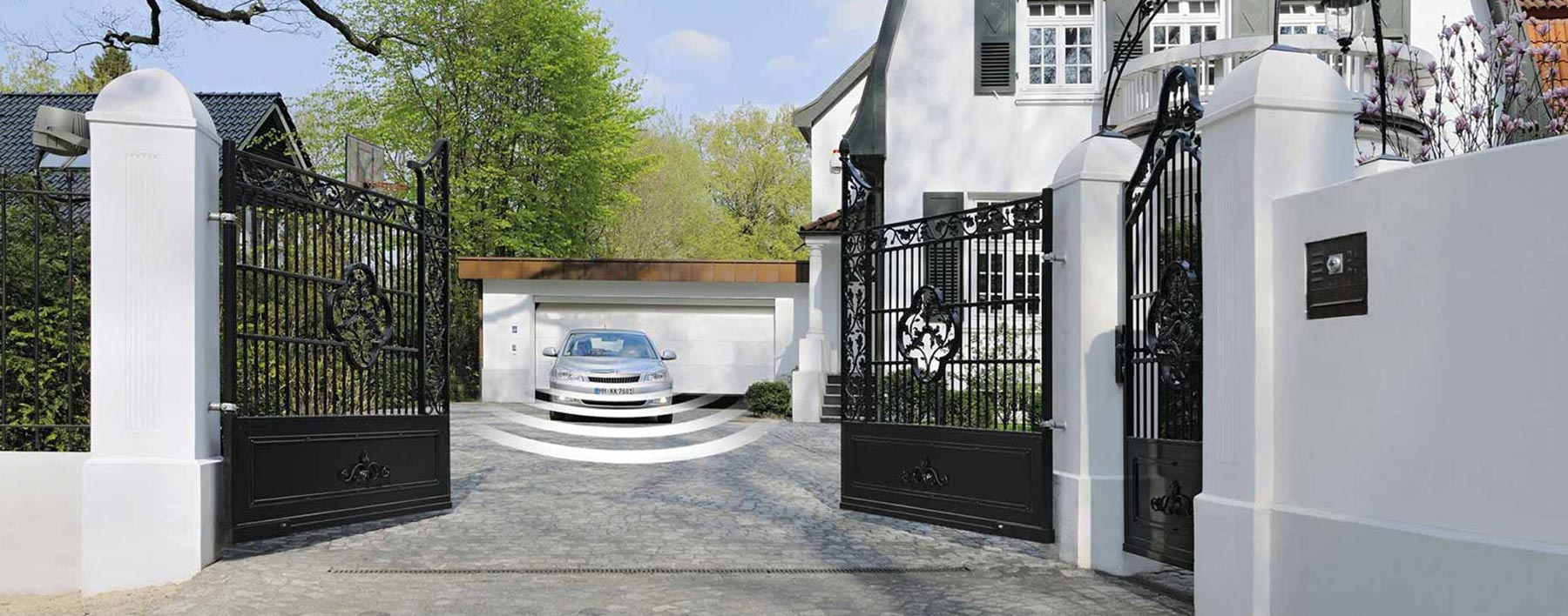 Auto fährt aus Hof heraus, während sich das elektrische Tor öffnet, was die praktische Automatisierung und Benutzerfreundlichkeit unserer AlmTor Produkte zeigt.