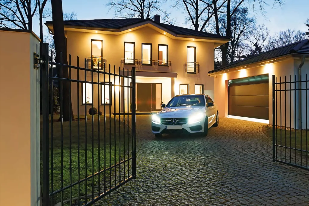 Stilvolles Hoftor von Almtor beleuchtet bei Dämmerung, einladend geöffnet für einen Mercedes vor einer eleganten Villa in Moers